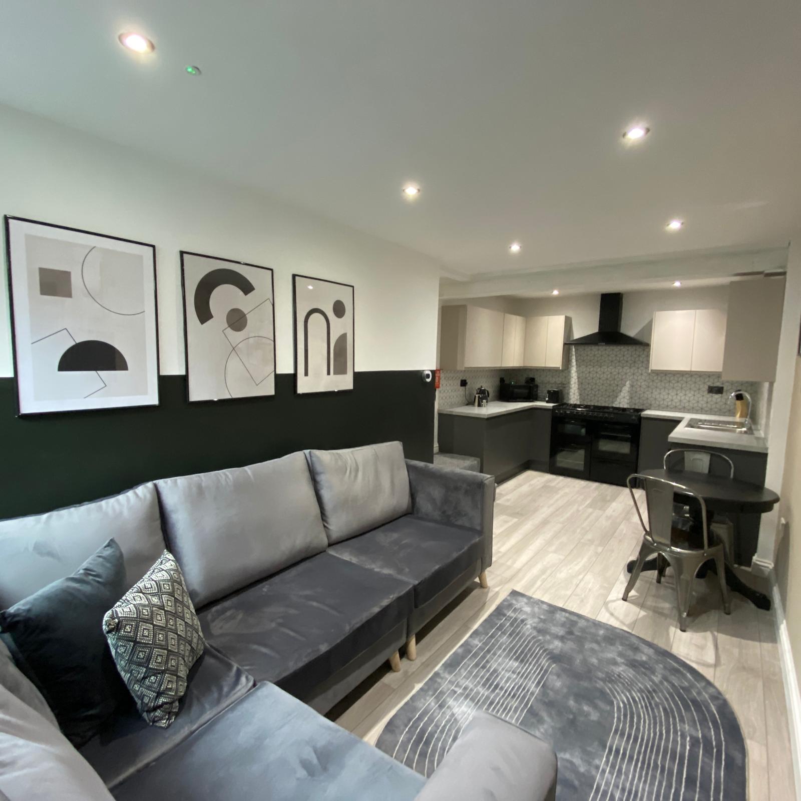 Open-plan living and kitchen space with grey sofa, dark green wall and modern kitchen