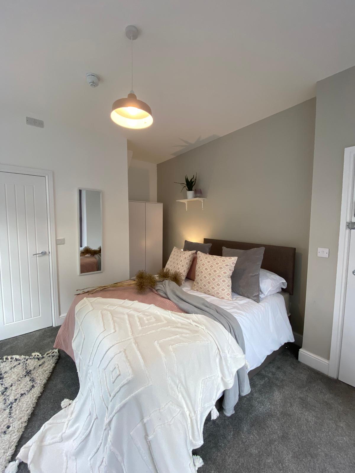 Neutral double bedroom with upholstered bed, throw cushions and bedside mirror