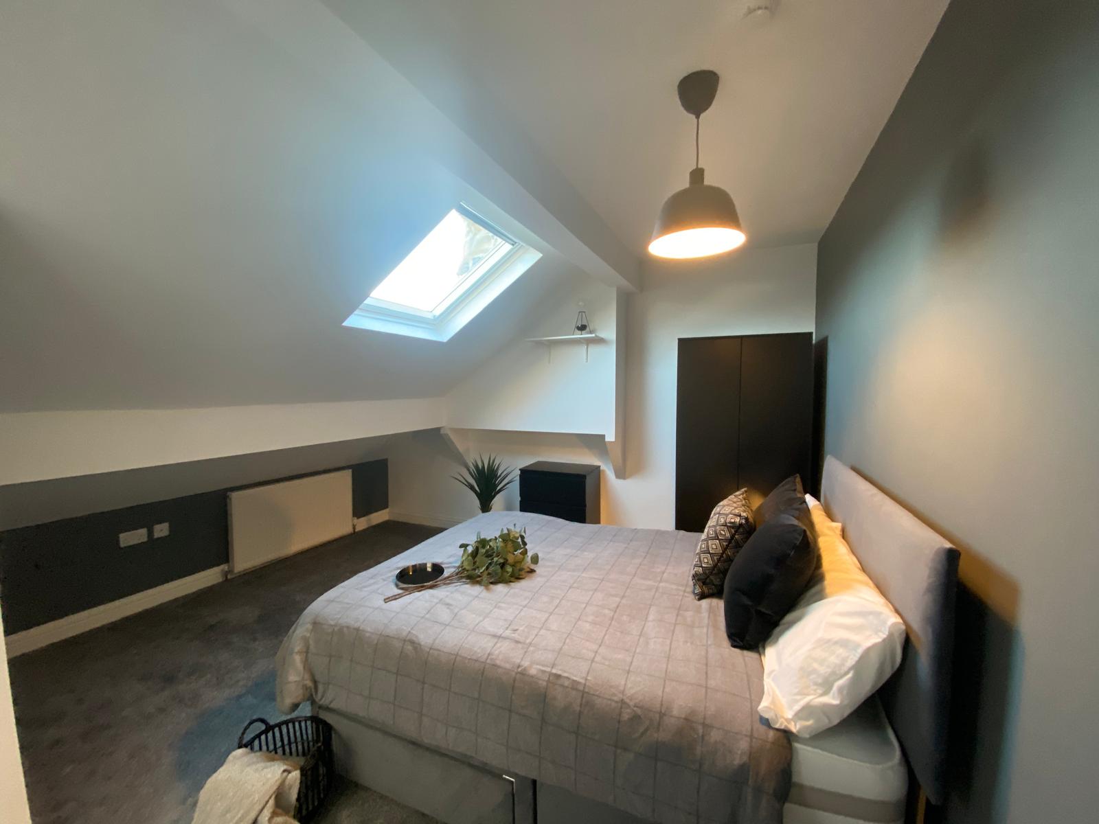 Loft-style double bedroom with skylight, neutral bedding and dark wardrobe