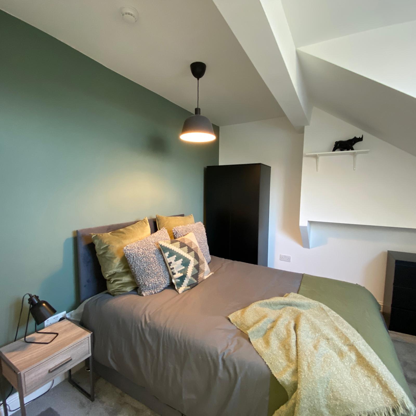Double bedroom with sage feature wall, mustard cushions, dark wardrobe and pendant light