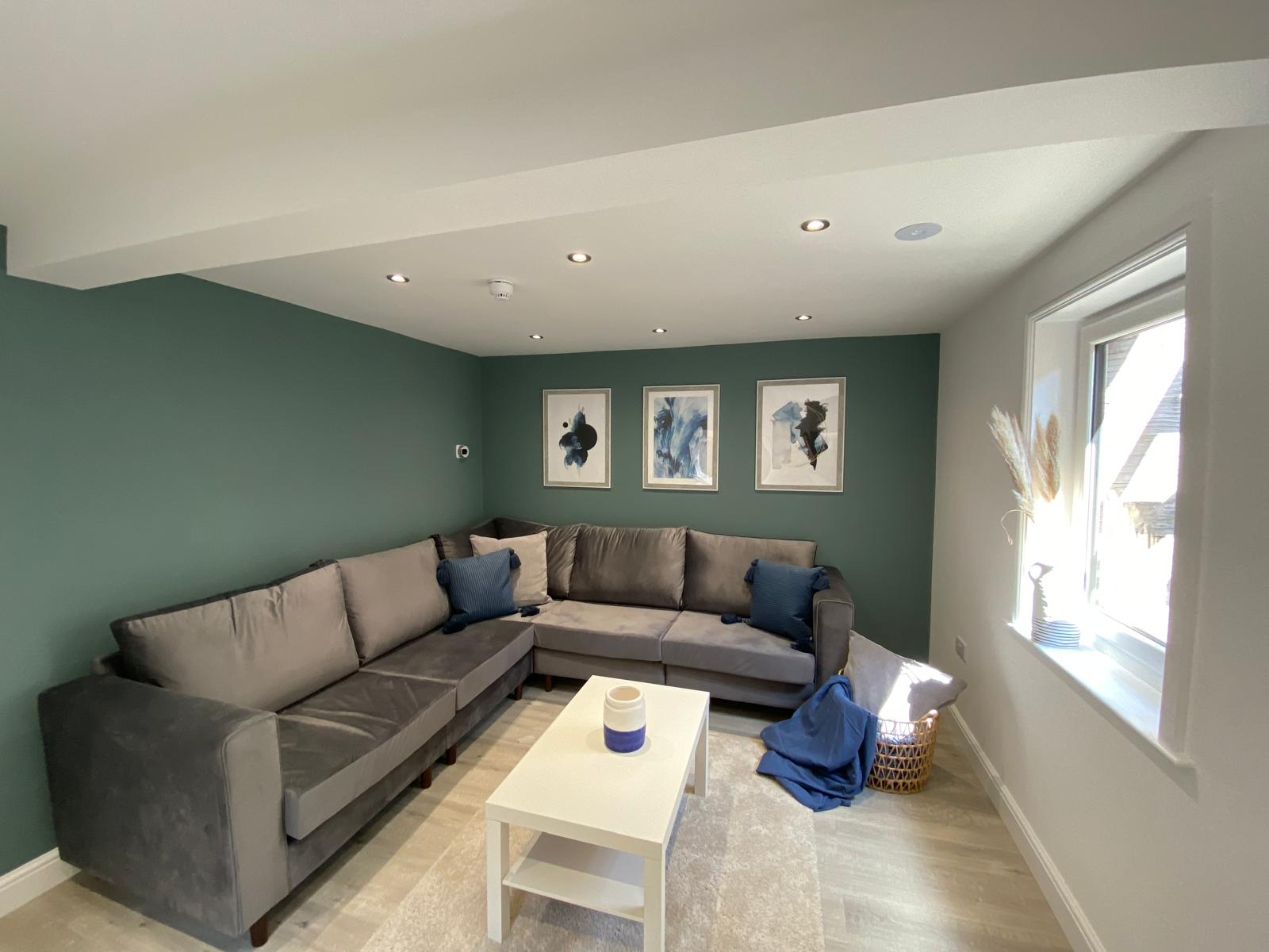 Living room with green feature wall, grey corner sofa and abstract wall art