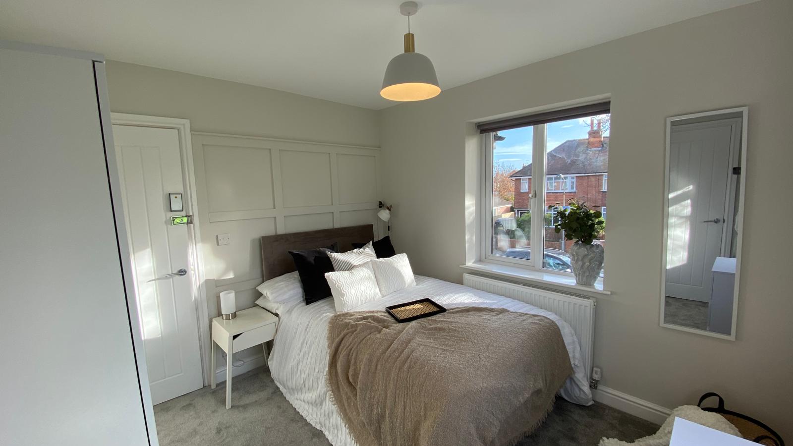 Bright double bedroom with window panelling, white bedding and soft throw